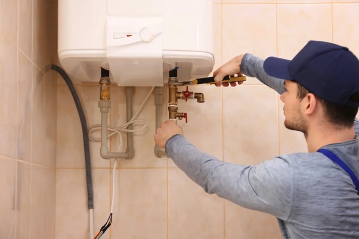 A technician installs or adjusts a tankless water heater mounted on a tiled wall, tightening plumbing connections beneath the unit during service in a New Jersey home.