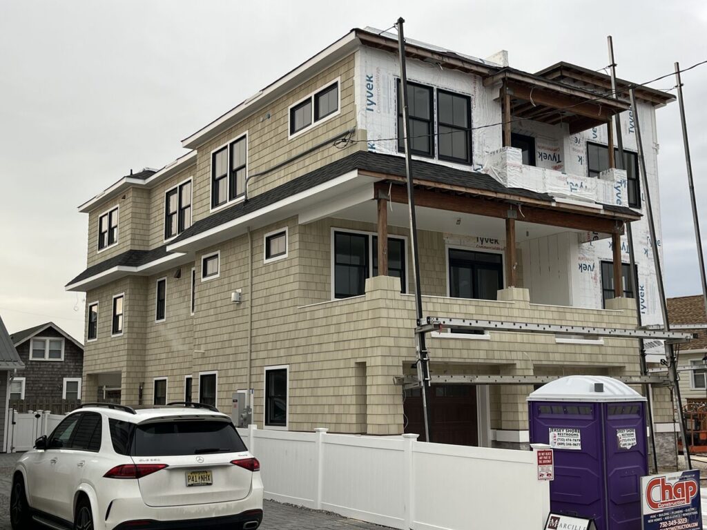 Rear view of a Chap Construction new home build in Seaside Park, NJ, featuring an elevated three-story design with shake siding, multiple balconies under construction, and a Chap Construction jobsite sign visible at street level.